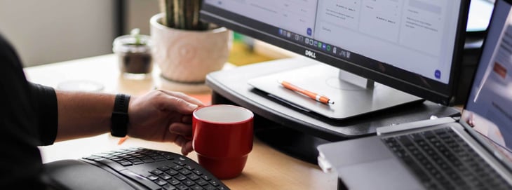 Image of a marketer working at a desk, holding a cup of coffee.