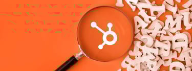 Magnifying glass highlighting the HubSpot logo on an orange background with scattered wooden letters, symbolizing HubSpot marketing terms.