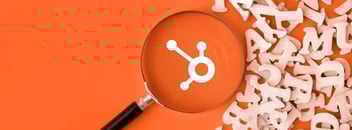 Magnifying glass highlighting the HubSpot logo on an orange background with scattered wooden letters, symbolizing HubSpot marketing terms.